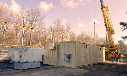 A CoverSix modular building unit being set by crane, with a backup generator staged on site.