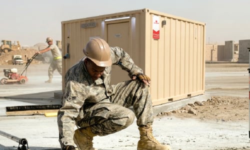) U.S. service member beside a CoverSix modular unit deployed at a forward operating base.